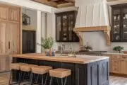 A kitchen with lots of natural wood tones, and a black island and white hood fan